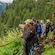 A group of people stand on a forest trail overlooking a valley and a glacier